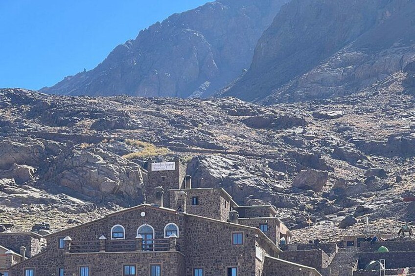 A mountainous landscape with a stone building featuring arched windows and a sign. 3