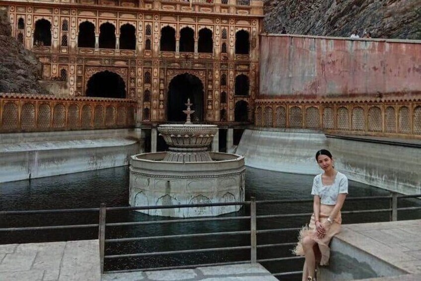 A person sitting on steps in front of a historic building with intricate architecture and a central fountain. 3
