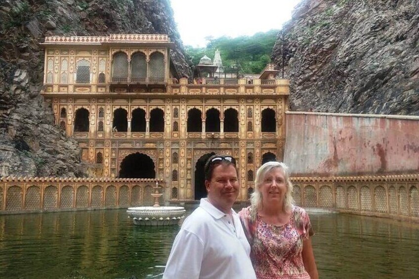 A historic building with intricate architecture, a body of water, and rocky cliffs. 5