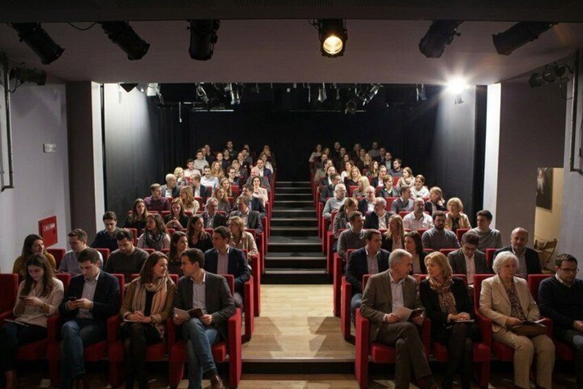 An auditorium with rows of red chairs and a stage at the front. 4