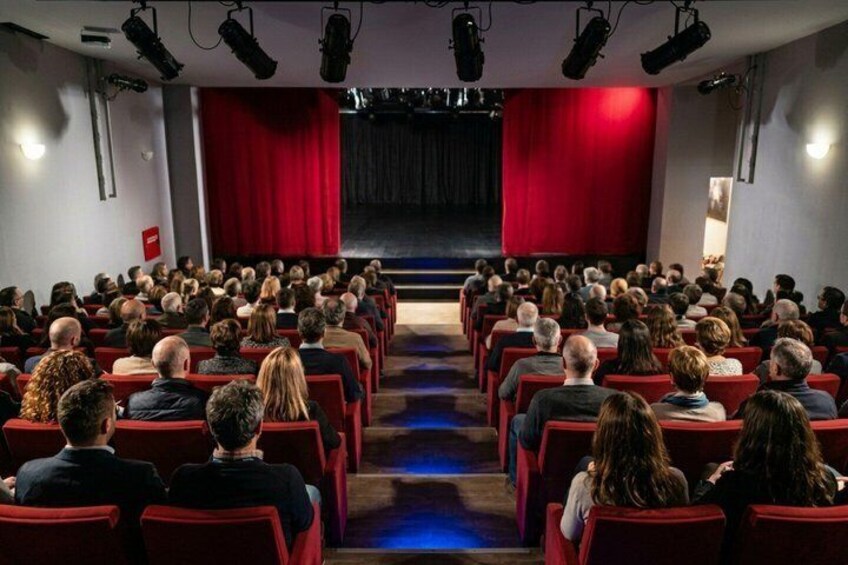 A theater with red seats and a stage. 5
