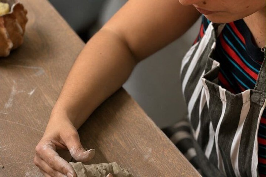 A person wearing a striped shirt and apron, working with dough on a wooden surface. 2