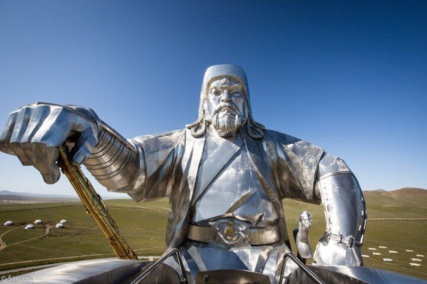 A large metallic statue of a figure holding a staff, set against a clear blue sky with a flat landscape in the background. 2