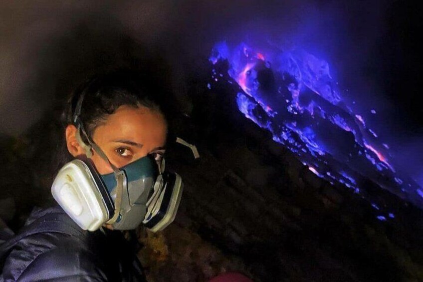 A person wearing a gas mask and a headlamp, standing in a cave with glowing blue lights. 1