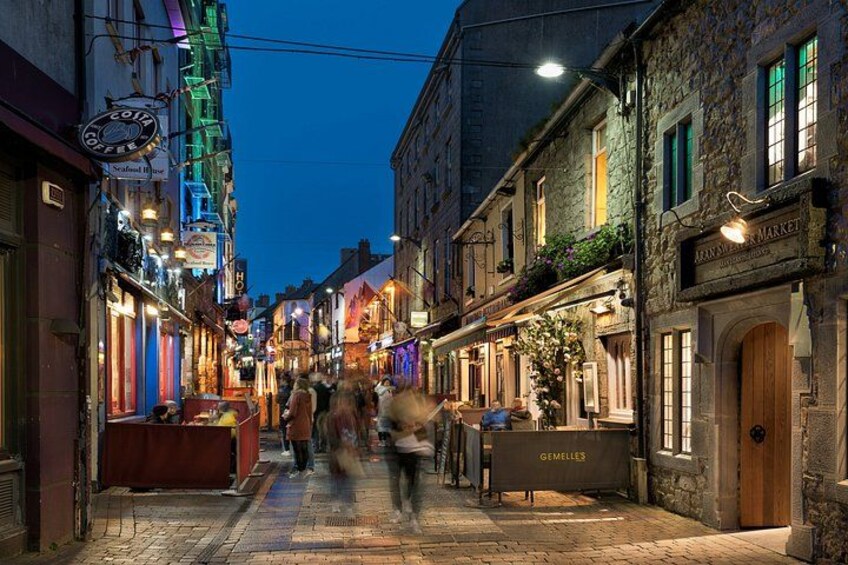 A cobblestone street lined with historic buildings, illuminated signs, and a few pedestrians. 2
