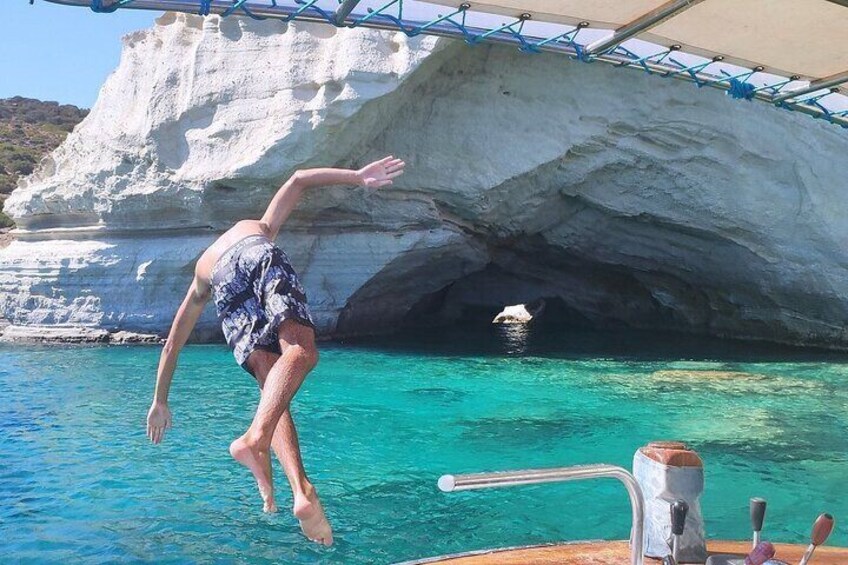 A person jumping off a boat into turquoise water with a rocky cliff in the background. 4
