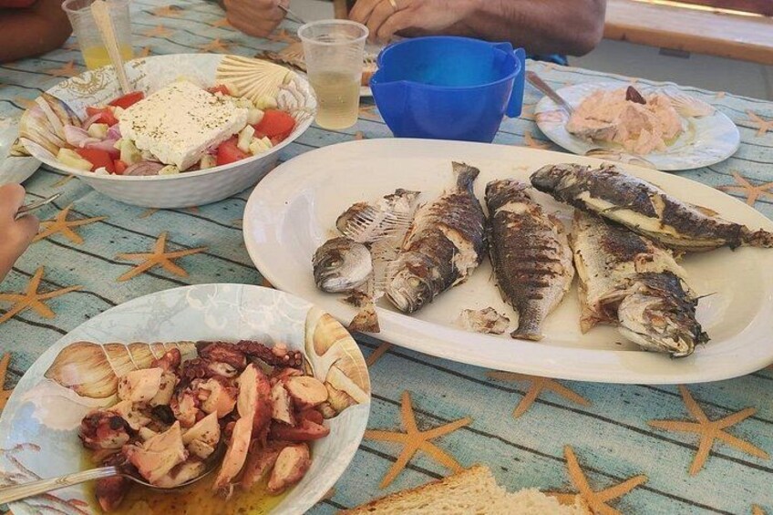A table with plates of grilled fish, a bowl of salad, and a drink. 3