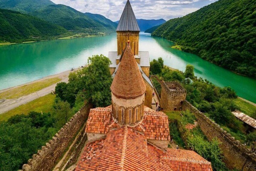 A church with a bell tower, surrounded by lush greenery and a river. 1