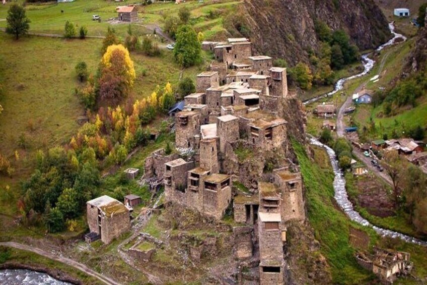 A cluster of ancient stone buildings atop a hillside, surrounded by a river and a small village. 5