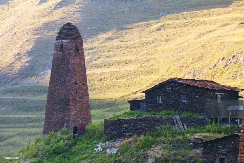 A brick tower and stone house in a hilly landscape. 4