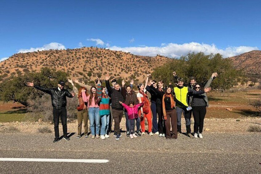A group of people standing on a road with a hilly landscape in the background. 1