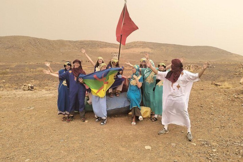 A group of people in traditional attire posing with a flag in a desert landscape. 4