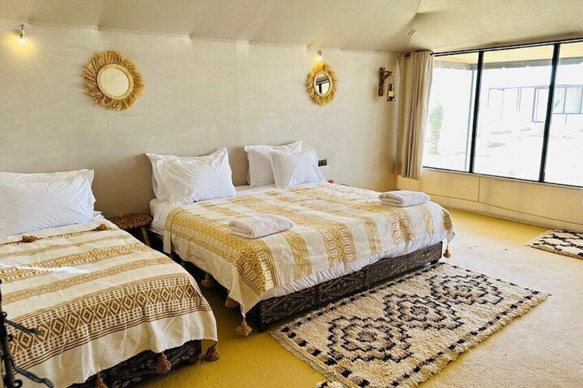 A hotel room with two beds, a large window, and a patterned rug. 5