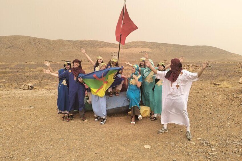 A group of people in traditional attire posing with a flag in a desert landscape. 2