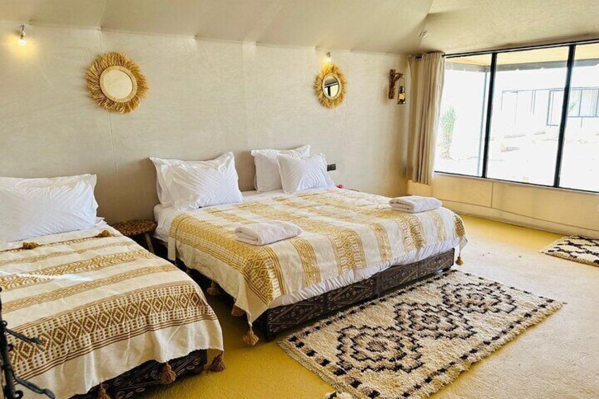 A hotel room with two beds, patterned bedding, a large window, and a decorative rug. 3
