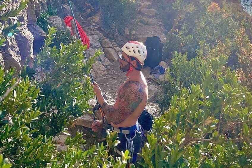 A person with a helmet and climbing gear, standing on a rocky terrain with vegetation. 3