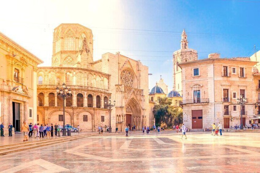 A historic square with a cathedral, a bell tower, and a fountain. 1