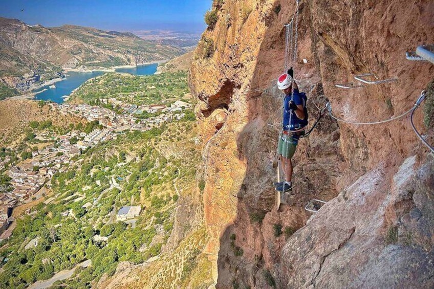 A person rock climbing a steep cliff with a town and lake in the background. 3