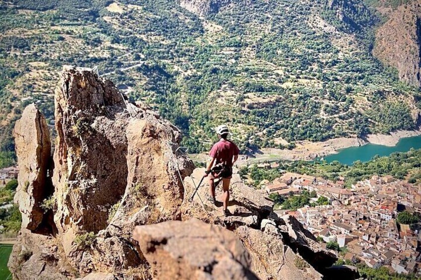 A person hiking on a rocky outcrop with a valley and lake in the background. 1