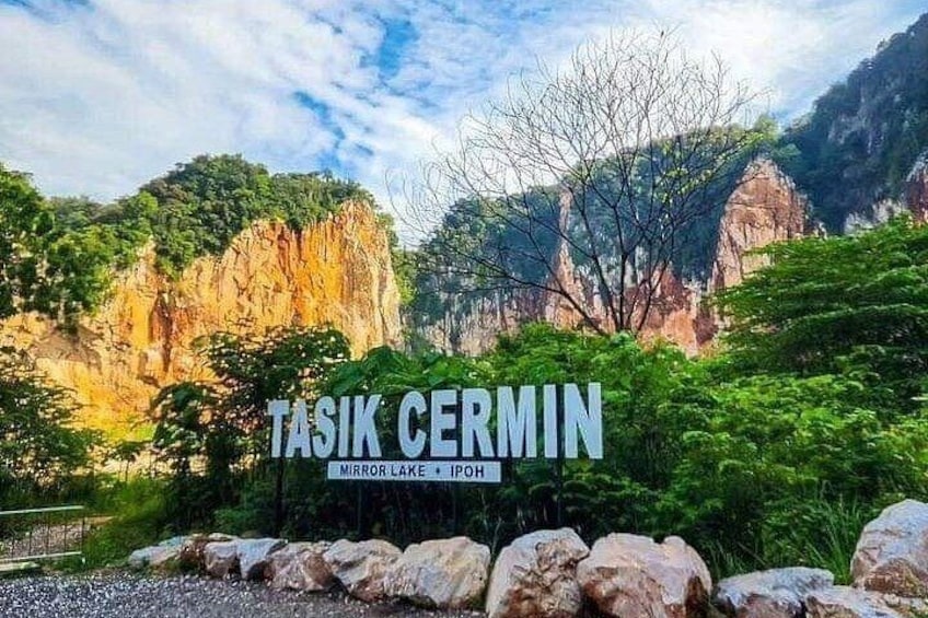 A mountainous landscape with a sign reading 'TASIK CERMIN MIRROR LAKE IPOH.' 1