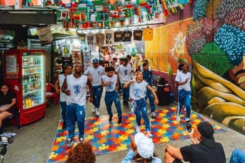 A group of people dancing on a colorful floor in a vibrant indoor setting with a mural and a poker machine. 1