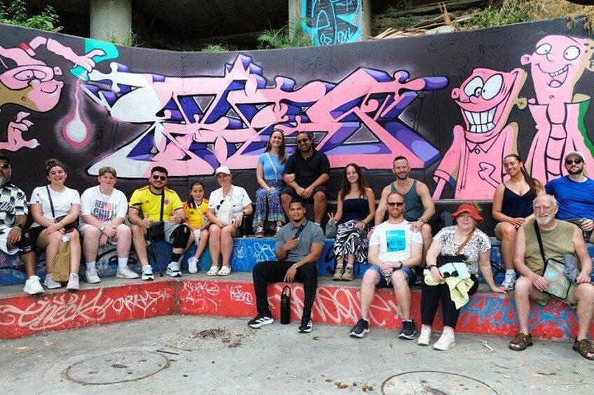 A group of people sitting on a bench in front of a colorful graffiti wall. 3