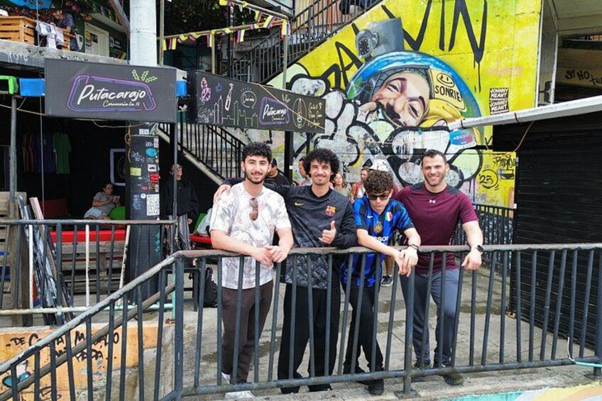A group of people standing near a graffiti-covered wall with a sign that reads 'Putacarajo.' 4
