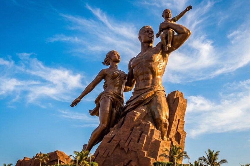 A large bronze statue of a man and a woman on a rock formation with palm trees in the background. 2