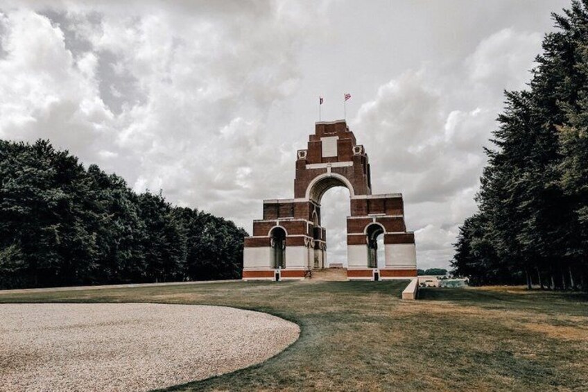 A large brick archway with a flag on top, surrounded by grass and trees. 5