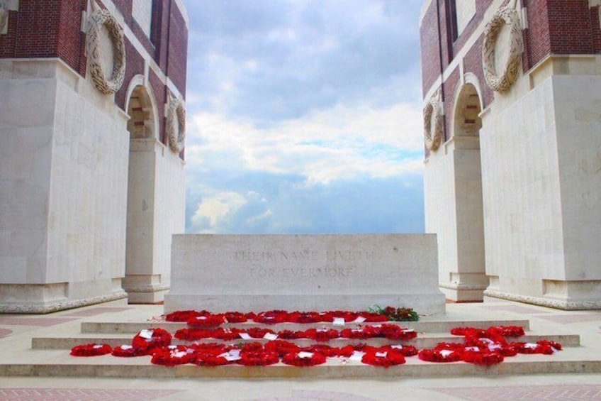 A memorial with a plaque and red flowers on steps. 1