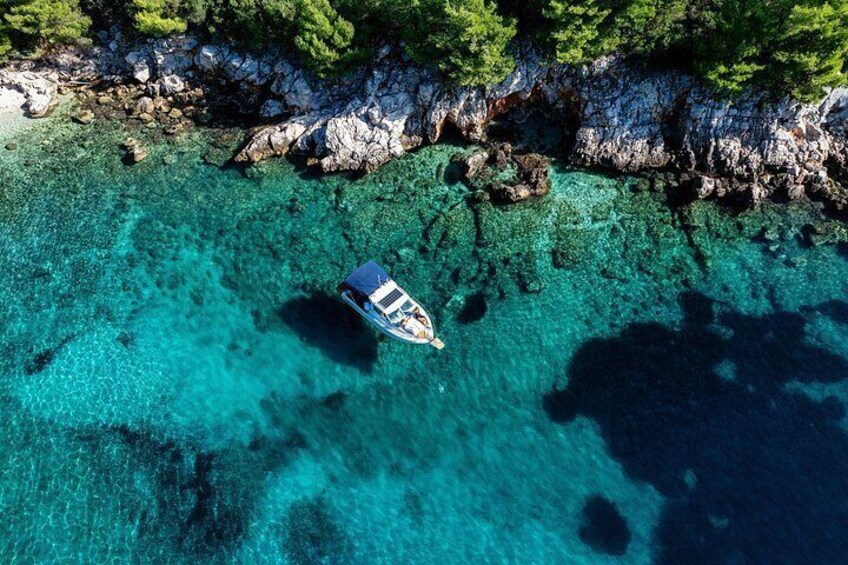 A boat on clear turquoise water surrounded by rocky coastline and green trees. 5