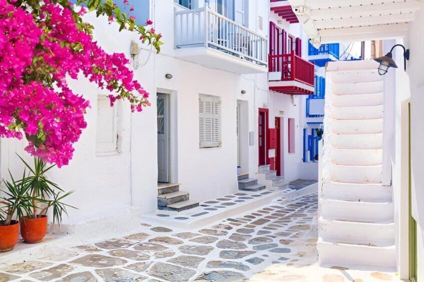A narrow street with white buildings, red doors, and blue balconies. 4