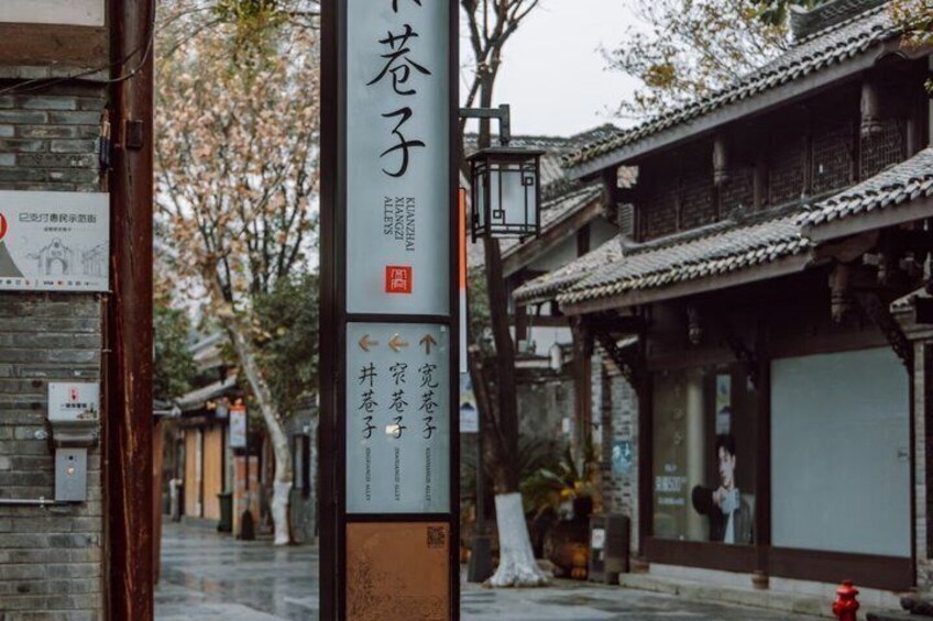 A traditional Chinese street with a signpost, buildings with tiled roofs, and a tree with blossoms. 3