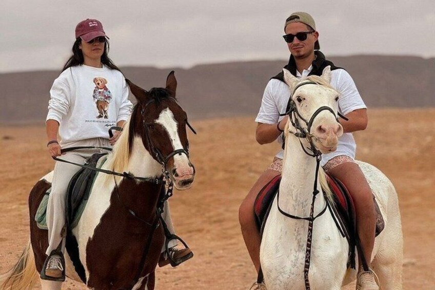Two people riding horses in a desert landscape. 1
