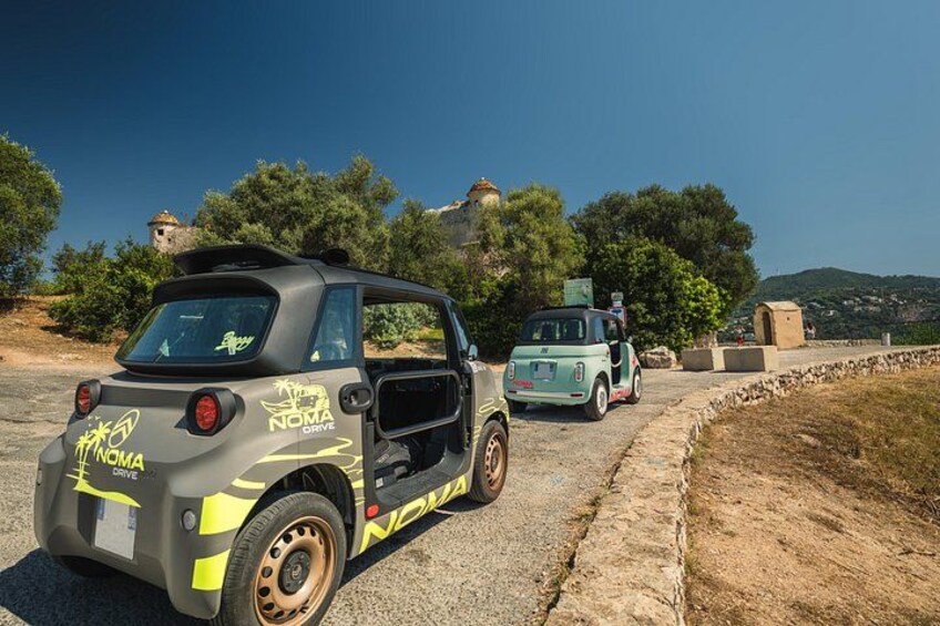 En mindre bil med 'NOMAD DRIVE' branding parkeret på en vej med et bjergrigt landskab i baggrunden. 4