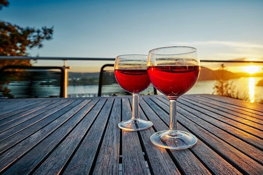 Two glasses of red wine on a wooden table with a sunset in the background. 3