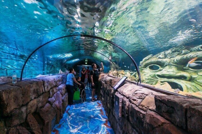 An underwater tunnel with a mural of a sea creature, a blue floor, and a group of people observing. 2