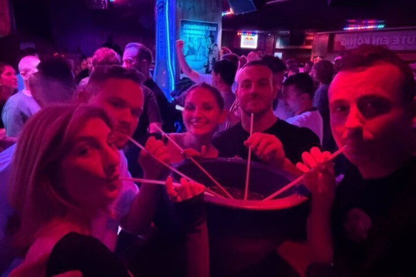 En grupp människor håller i ett stort, platt, vitt föremål med flera handtag. Det kan vara en dekorativ artikel eller en möbel. Bilden är tagen i en svagt upplyst inomhusmiljö med rött ljus. 4