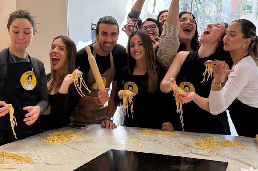 A group of people cooking spaghetti in a kitchen. 1