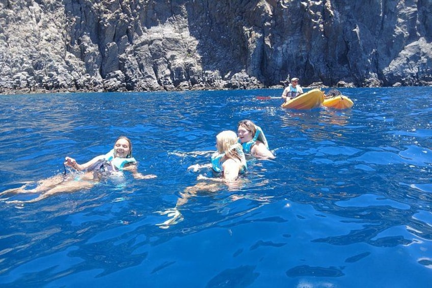 People swimming in a clear blue sea with rocky cliffs in the background. 4