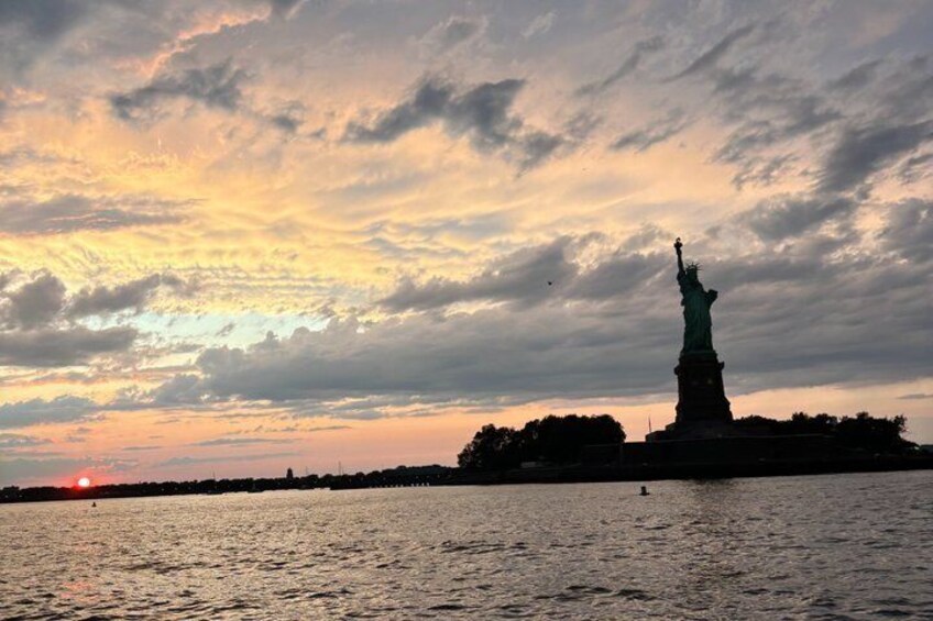 The Statue of Liberty at sunset with clouds in the sky and water in the foreground. 1