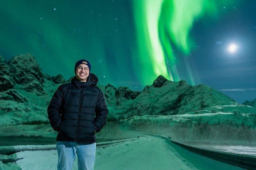 A person standing on a road with mountains in the background and the Northern Lights in the sky. 4