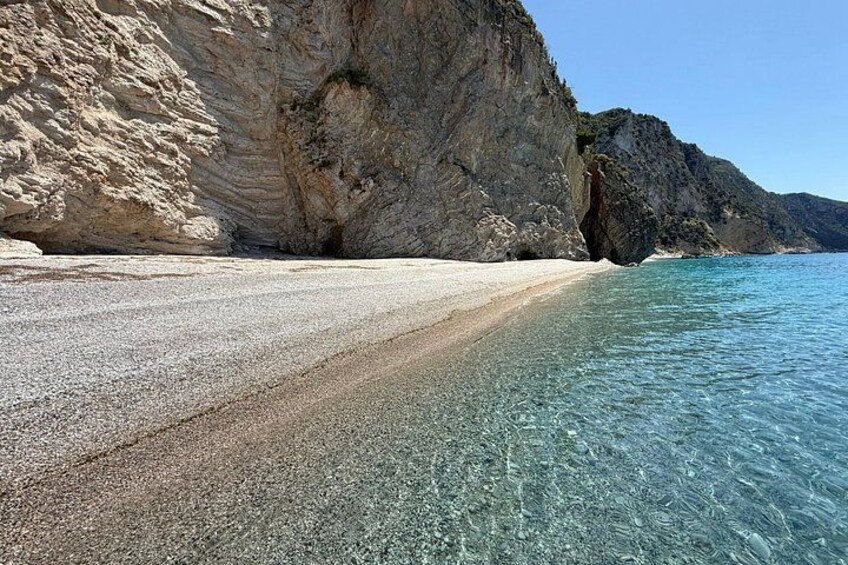 A beach with clear water, a rocky cliff, and a clear sky. 3