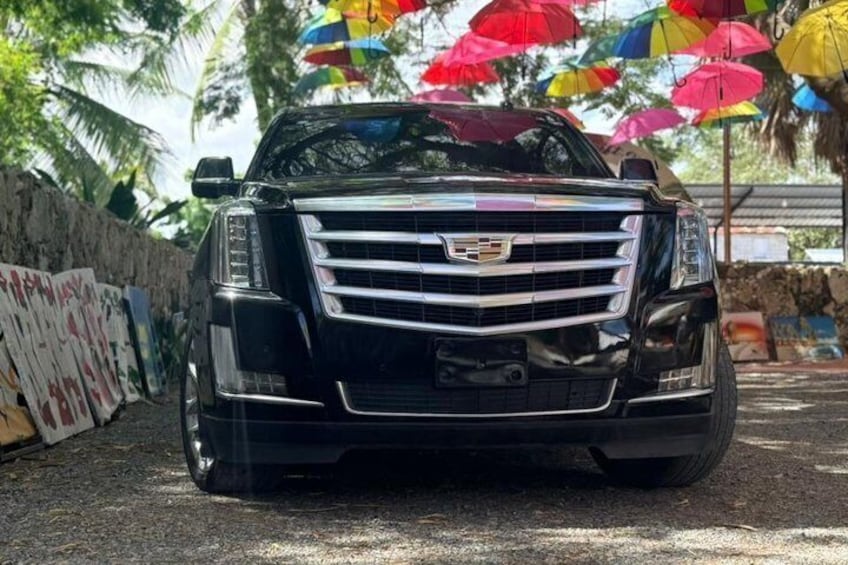 A black Cadillac SUV parked on a street with colorful umbrellas overhead. 1