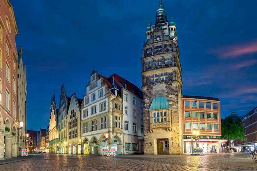 A cobblestone street lined with historic buildings, including a prominent tower with a spire. 3