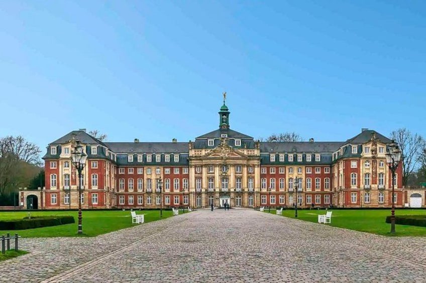 A large, historic building with a symmetrical facade, a central entrance, and a paved courtyard. 2
