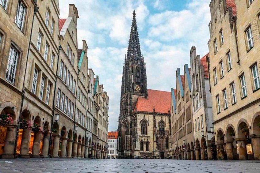 A historic square with a prominent church spire, arched buildings, and cobblestone pavement. 5
