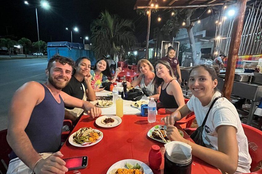 A group of people dining at an outdoor restaurant with red tables and chairs. 4