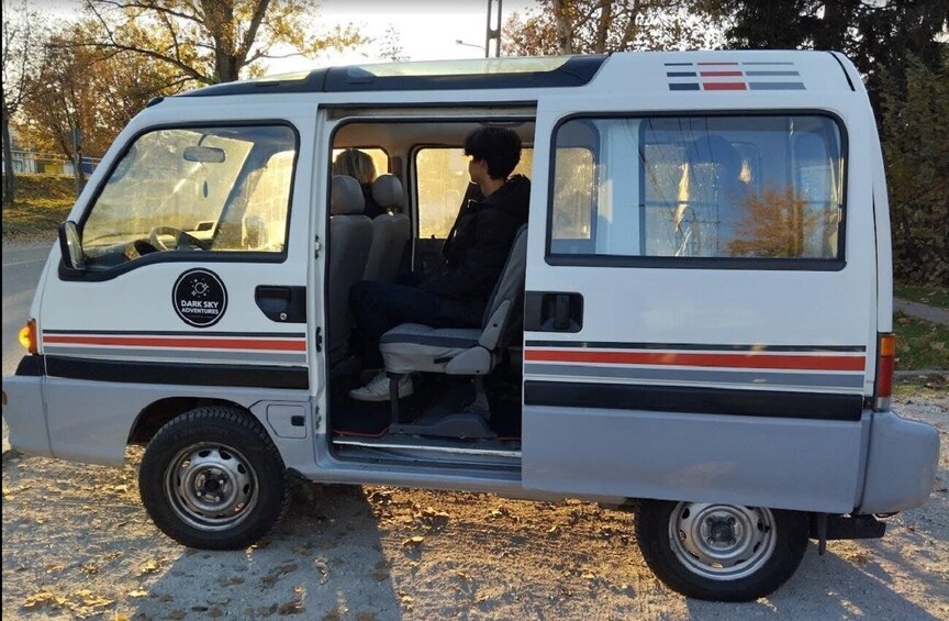 A white van with a logo on the side, parked on a gravel surface with trees in the background. 4