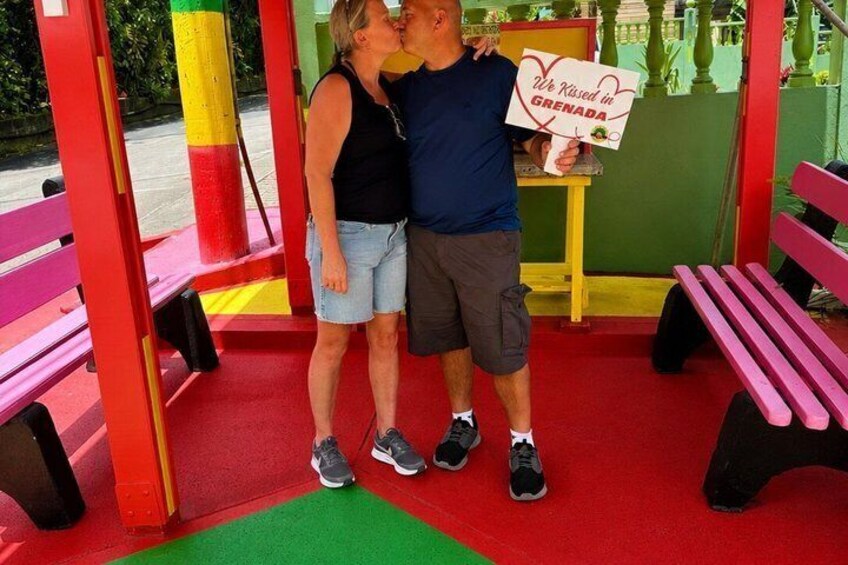 A couple kissing in a playground with a sign that reads 'We Kissed in Grenada.' 2